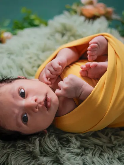 An awake and curious baby swaddled in a yellow wrap, looking up at the camera.