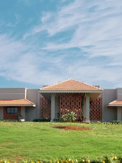 A frontal view of the Ratnagiri VTC, nestled in a green landscape. The building's design is context-responsive, using natural ventilation techniques and local laterite stone to create a sustainable and culturally rooted institution.