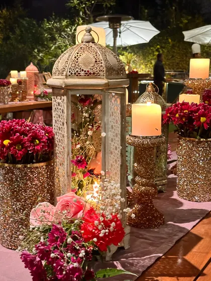 A close-up of a table centerpiece featuring a glittery vase, a lantern, and fresh flowers.