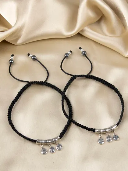 A pair of black cord anklets or bracelets with dangling silver coin charms.