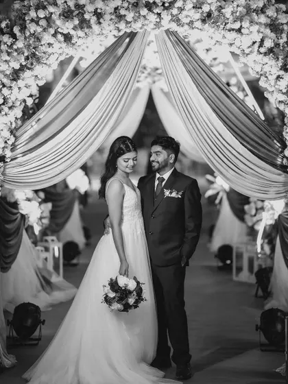 A classic black and white portrait of the couple under a draped archway. The monochrome tones emphasize the elegant lines of the decor and their attire.