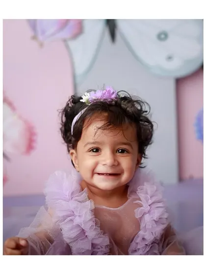 A big, happy smile from the birthday girl in her purple butterfly-themed dress.