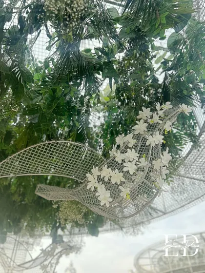A delicate detail of a wire mesh bird sculpture adorned with white flowers, hanging amidst lush greenery. This small touch adds a whimsical and artistic element to the botanical theme.
