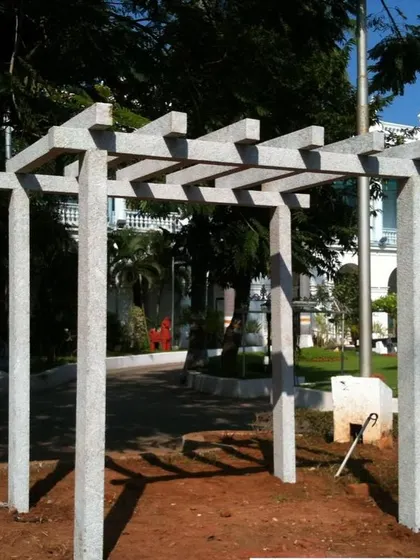 A minimalist stone pergola with clean lines, perfect for a modern garden design. The structure casts interesting shadows on the ground.