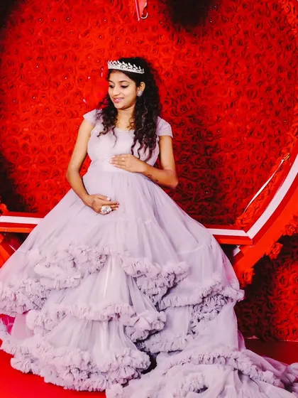 A lovely maternity portrait of a woman in a light purple ruffled gown with a tiara, seated inside our red heart studio prop.
