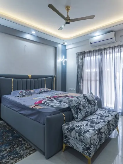 A modern bedroom design in a cool blue and grey palette with subtle gold accents. The false ceiling with cove lighting and stylish butterfly-shaped wall sconces add a touch of glamour and sophistication.