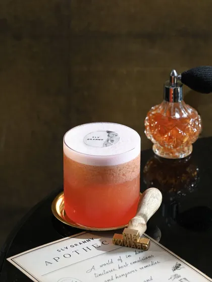 The Hotel Du Lac, perfectly styled. This foamy, pink-hued cocktail is served with my custom 'Apotheca' card, hinting at the secret remedies and stories behind my drinks.