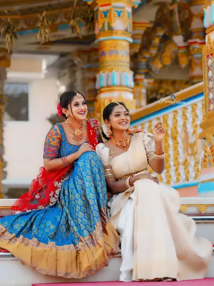 A beautiful shot of two friends in our rental half sarees, one in blue and red, the other in classic cream and gold.