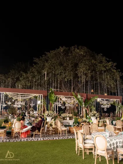 A wide evening shot of a stunning outdoor wedding reception, with multiple seating areas, grand decor structures, and magical lighting from fairy lights in the trees.