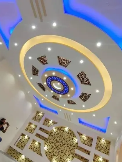 This photo shows the scale of my work. I am seen here working on a large, ornate wall and ceiling project, combining intricate patterns with bold blue and yellow lighting.