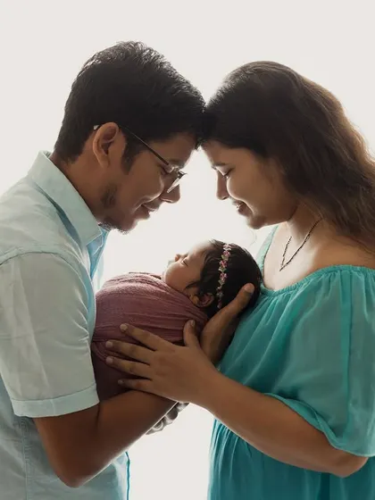 A new family of three, bathed in soft, bright light. This high-key portrait in color shows the warmth and love surrounding their new baby.