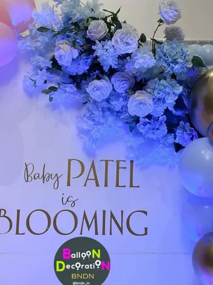 A close-up of the "Baby Patel is Blooming" personalized backdrop, combining elegant script with beautiful blue floral arrangements.