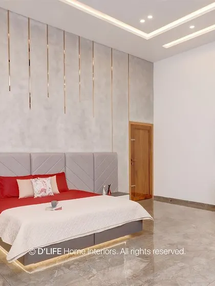 A spacious bedroom with a striking red bedspread, a textured grey wall with metallic inlays, and a sleek white study unit. The design is bold, modern, and luxurious.