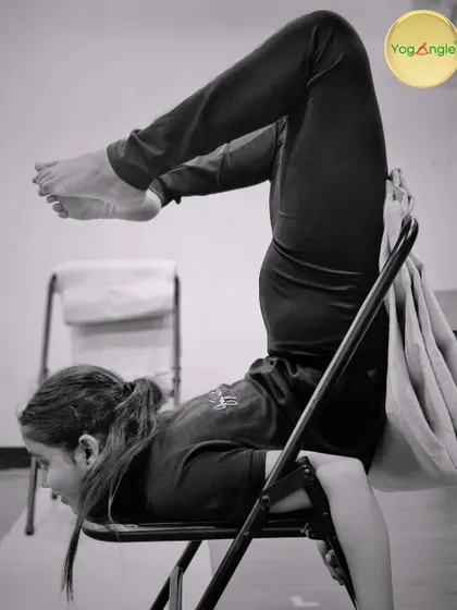 This black and white shot captures a young student in a supported shoulder stand variation using a chair. Props make yoga accessible to all ages, helping build body awareness and confidence from an early age.