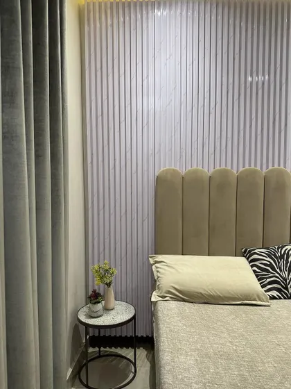 A close-up of the bedroom wall design in Jasola, showing the texture of the fluted panel next to the soft, scalloped velvet headboard.