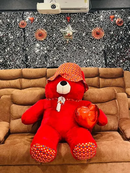 A cute teddy bear sits on our plush recliner, part of a sweet surprise setup with a shimmer wall background.