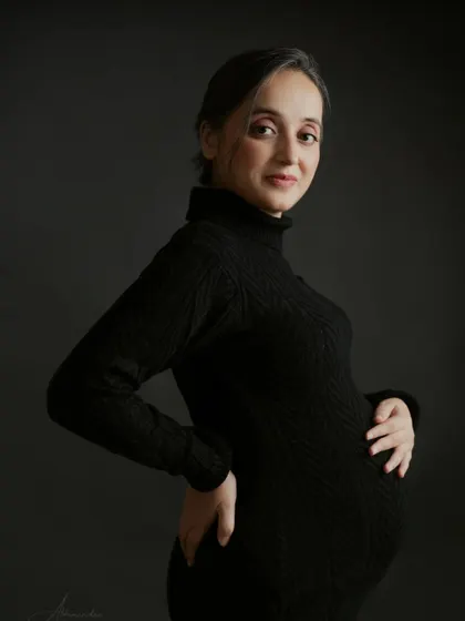 A classic and moody portrait. The mom-to-be looks directly at the camera, exuding quiet confidence in a black turtleneck-style bodycon dress.