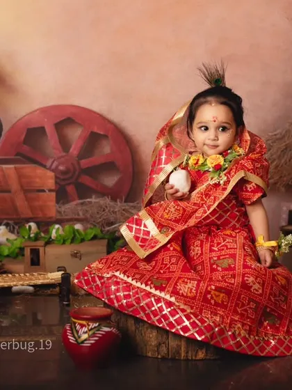 Our little Radha, holding a ball of makhan, looks absolutely divine in her traditional red attire.