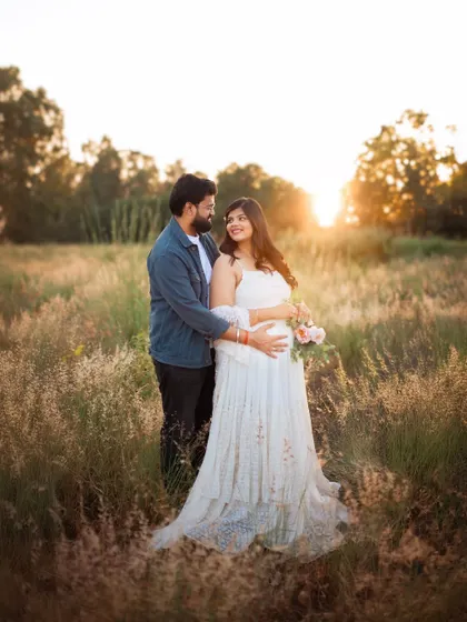 A wider shot showcasing the beautiful landscape and the couple's connection. The flowing dress and the tall grasses add a sense of romance and freedom to this outdoor pregnancy shoot.