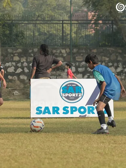 A player dribbles past the Sar Sportz branding board.