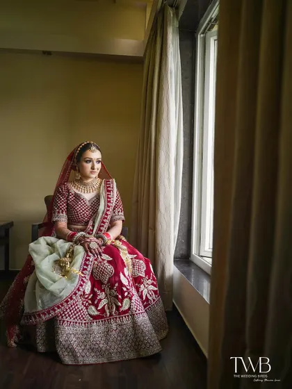 A pensive bridal portrait by the window. The natural light beautifully illuminates the bride in her red lehenga, capturing a moment of calm and anticipation before the ceremony.
