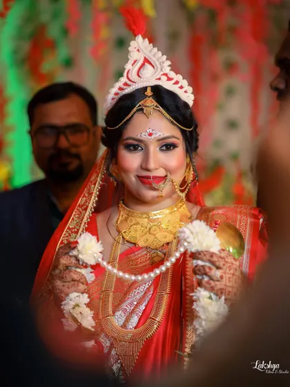 A happy portrait of the Bengali bride during the wedding ceremony. She is holding the 'shubho drishti' garland, smiling brightly for the camera.