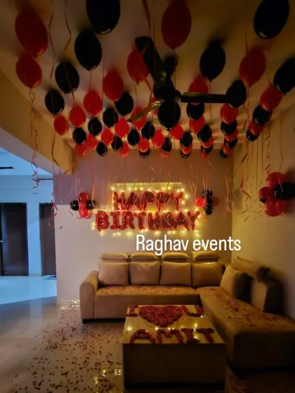 A romantic birthday surprise for Amit. The decoration includes red and black balloons, a 'Happy Birthday' foil banner, and his name written with rose petals on the coffee table.