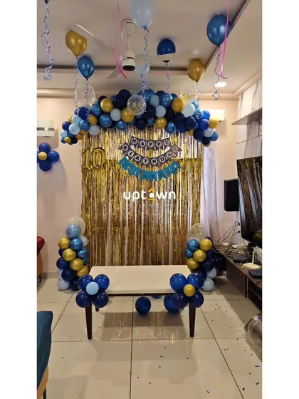 A simple home birthday decoration with a gold foil curtain and blue and gold balloons.