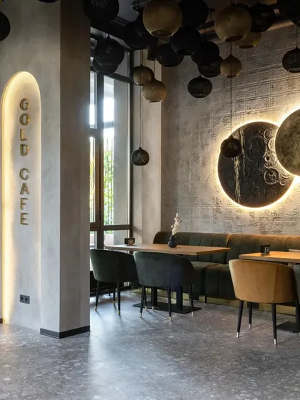 The "Gold Cafe" interior uses a sophisticated palette of grey, black, and gold. The backlit wall art and signage create a warm glow against the textured concrete walls.