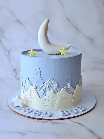 A simple and beautiful cake with a moon and mountains theme. The periwinkle blue and buttercream painting create a serene landscape.