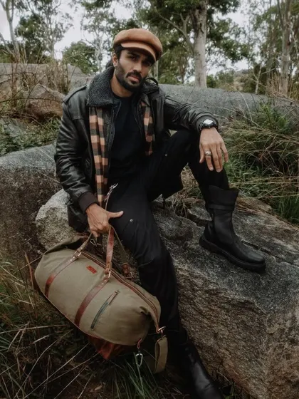 A lifestyle shot from the Loki Craft India campaign. The styling combines a leather jacket, plaid scarf, and sturdy boots to create a complete look that embodies the brand's adventurous and durable spirit.