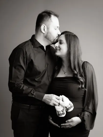A classic black and white portrait of a couple celebrating their journey to parenthood. The dad-to-be's tender kiss and the tiny "Future Mom" socks add a sweet touch.