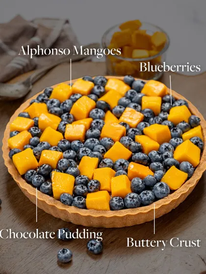 A breakdown of my Mango and Blueberry Tart. It features a buttery crust, rich chocolate pudding, and a generous topping of sweet Alphonso mangoes and fresh blueberries.