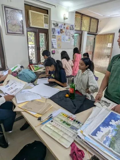 A typical day at the studio, with students deeply engaged in their work. An instructor is reviewing a student's landscape paintings while others continue with their drawing and painting exercises.
