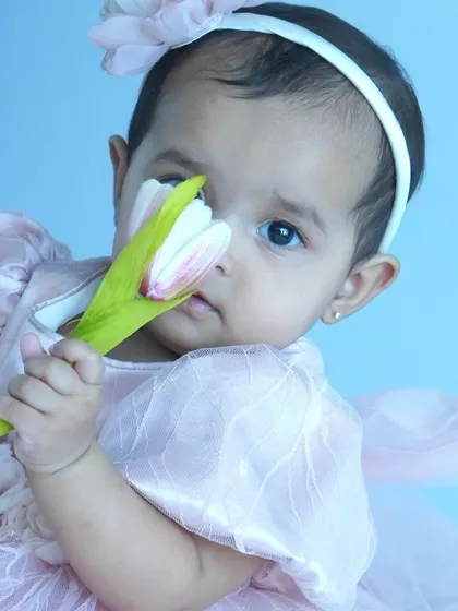An adorable portrait of a baby girl holding a flower close to her face. This shot captures the delicate features and innocent curiosity of a baby during a themed photoshoot.