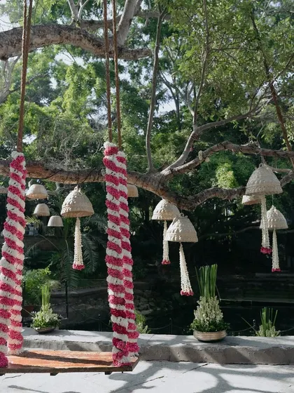 A swing decorated with red and white flowers, with hanging bell-shaped decor in the background.