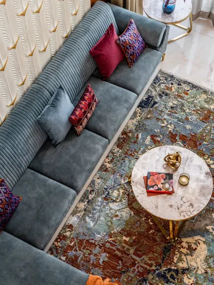 An overhead view of the living area highlights the layering of colors and textures. The abstract rug grounds the space, while the custom sofa and marble coffee table add layers of comfort and luxury.