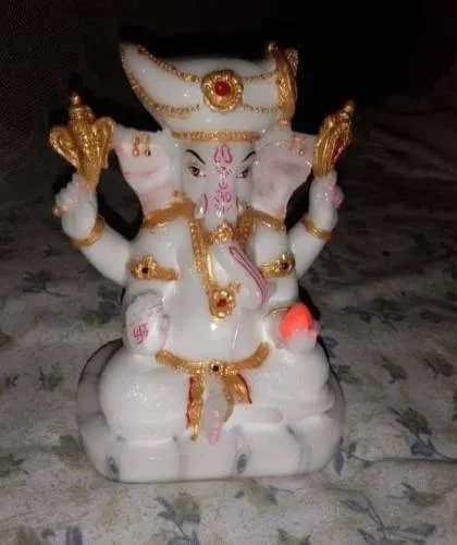 A small, intricately detailed statue of Lord Ganesha in white and gold, suitable for a home altar or as a decorative piece.