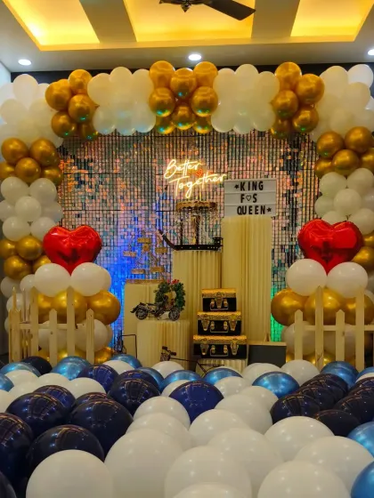 This is the gold, white, and blue anniversary decoration under bright, warm lighting. The heart-shaped balloons are a popular add-on for romantic events like anniversaries or proposals.