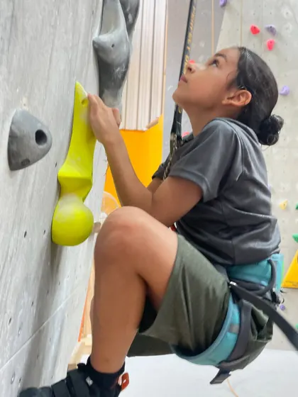 Another young climber hangs on, determined to finish the route. The supportive atmosphere encourages everyone to push their limits.