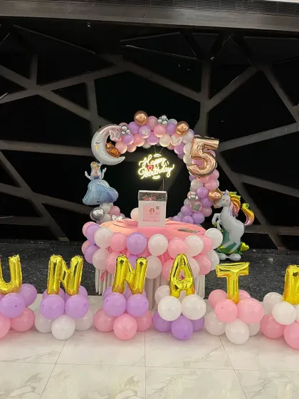 A whimsical Unicorn and Princess theme for a 5th birthday. The decor features a balloon-wrapped table, a circular balloon arch with a moon accent, and foil letter balloons spelling out the name.