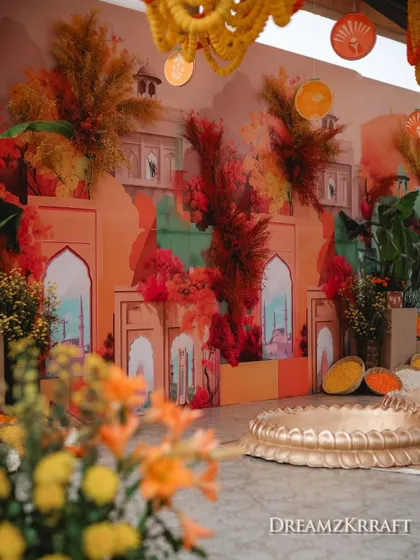 The Haldi stage backdrop, featuring a colorful mural and explosive floral arrangements in shades of red and orange.