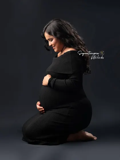 A kneeling portrait in a simple black dress, creating a timeless and elegant silhouette against the dark backdrop.