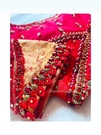 A close-up of a heavily embellished blouse sleeve, featuring 3D floral details, beads, and zardosi work on a vibrant red fabric.