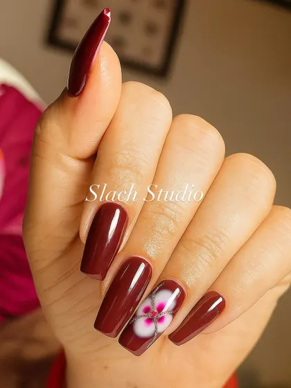 A closer look at the hand-painted flower on these long, coffin-shaped nail extensions. The blend of white and pink creates a realistic, layered effect against the bold maroon base.