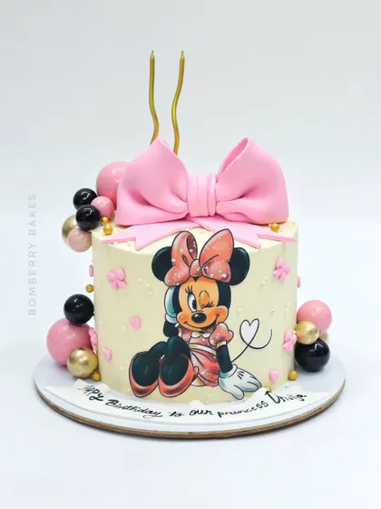 An adorable Minnie Mouse cake featuring a hand-painted illustration, a large pink fondant bow, and balloon decorations.