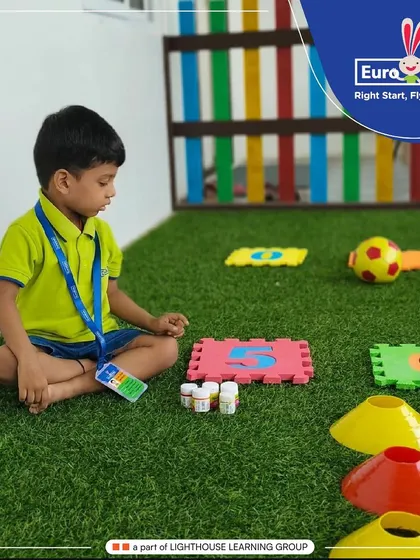 A child sits on the floor surrounded by number puzzles, cones, and other learning materials. This setup for an experiential math activity allows children to explore numbers and quantities at their own pace.