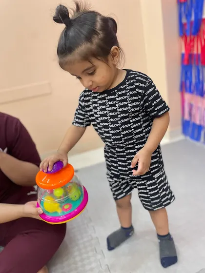 A toddler stands and plays with a spinning toy, practicing balance and coordination while engaging in focused play.