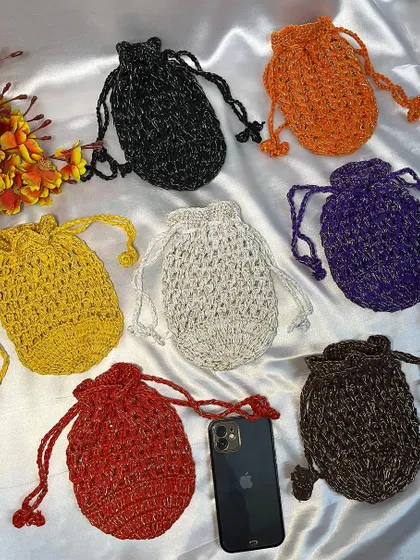 This image displays a variety of my handmade crochet potli bags in seven different shimmering colors, including black, orange, and purple. An iPhone is shown for size reference.
