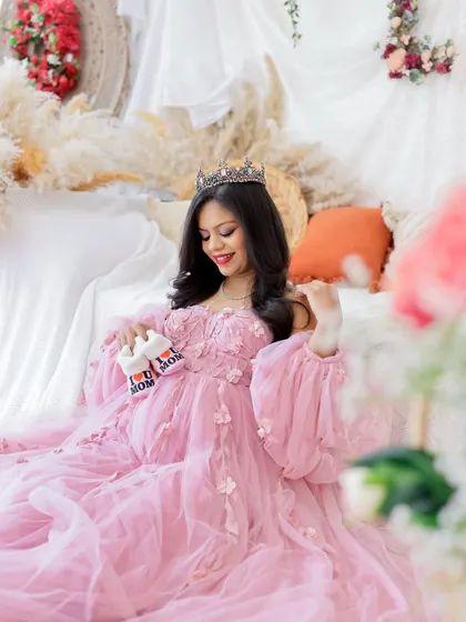 A sweet and regal portrait. The mom-to-be wears a tiara and a beautiful pink gown, holding tiny "I love Mom" booties.
